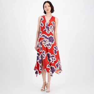 A red midi dress with a v-neckline featuring a large purple and white floral print, asymmetrical hem, and sleeveless design. The model is wearing white strappy heels.
