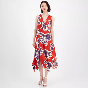 A red midi dress with a v-neckline featuring a large purple and white floral print, asymmetrical hem, and sleeveless design. The model is wearing white strappy heels.
