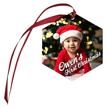 Hexagon-shaped Christmas ornament featuring a baby in a Santa hat with \“Owen's First Christmas\“ text, accompanied by a red ribbon.
