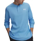 A person wearing a light blue Under Armour Henley shirt with a logo on the chest and black pants, hands in pockets.
