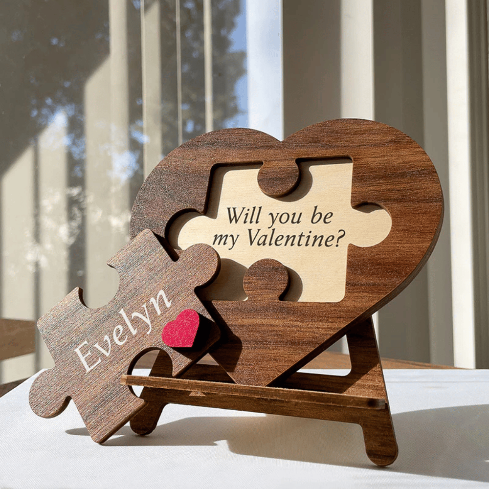 A wooden heart-shaped puzzle with a piece that reads \“Evelyn\“ and a heart symbol. The puzzle displays the message \“Will you be my Valentine?\“