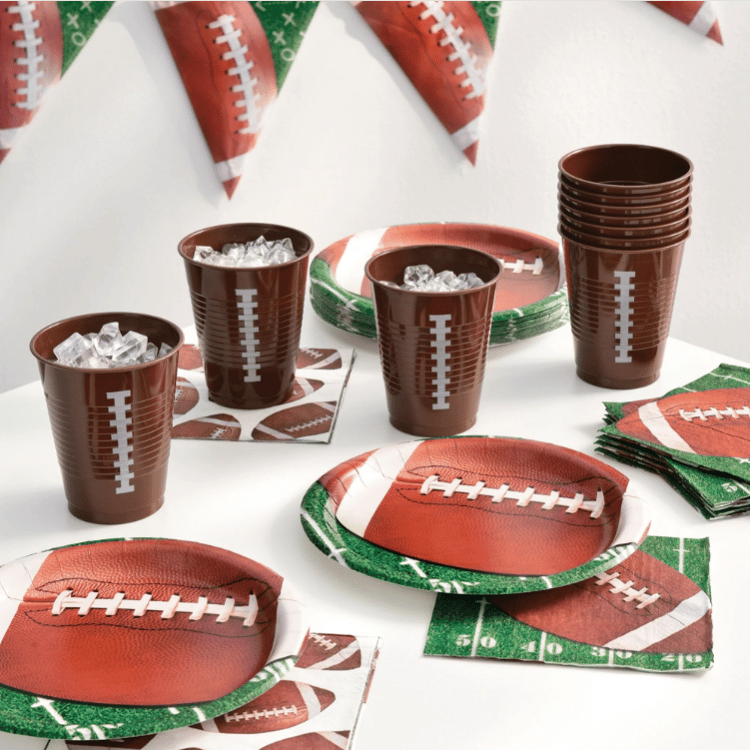 Football-themed party supplies including cups, plates, napkins, and banners, all featuring designs resembling footballs and fields.