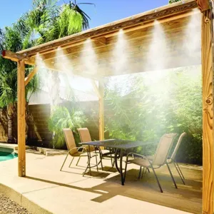 A pergola with an integrated outdoor misting system provides cooling over a patio area with a table and chairs, set beside a pool and surrounded by lush greenery.