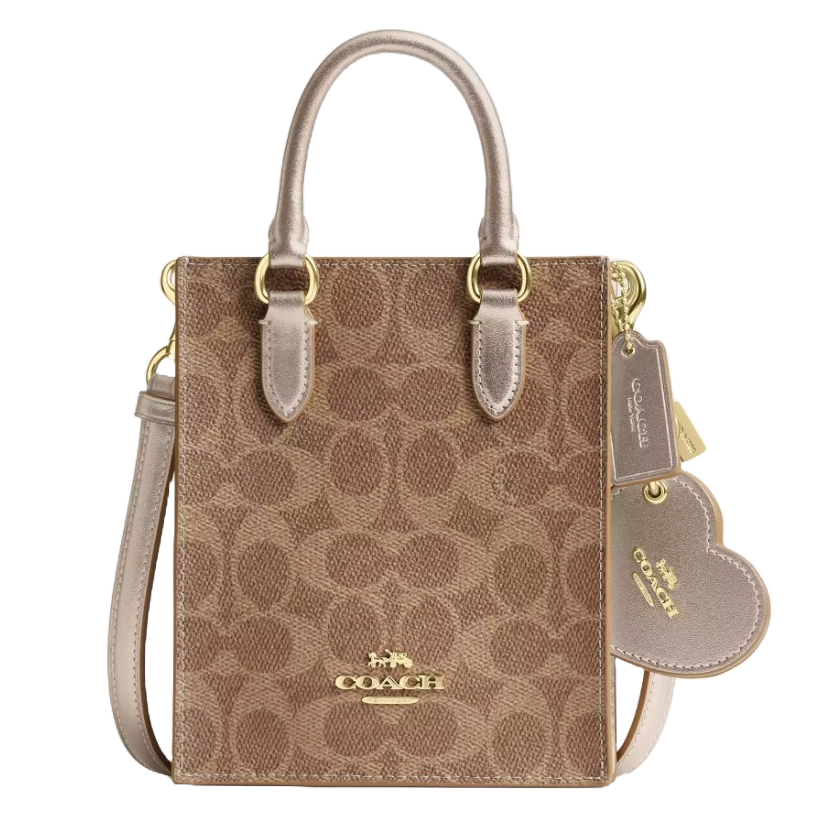 A Coach tote bag featuring a brown monogram pattern, gold hardware, dual top handles, a detachable shoulder strap, and a heart-shaped tag accessory.