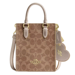 A Coach tote bag featuring a brown monogram pattern, gold hardware, dual top handles, a detachable shoulder strap, and a heart-shaped tag accessory.