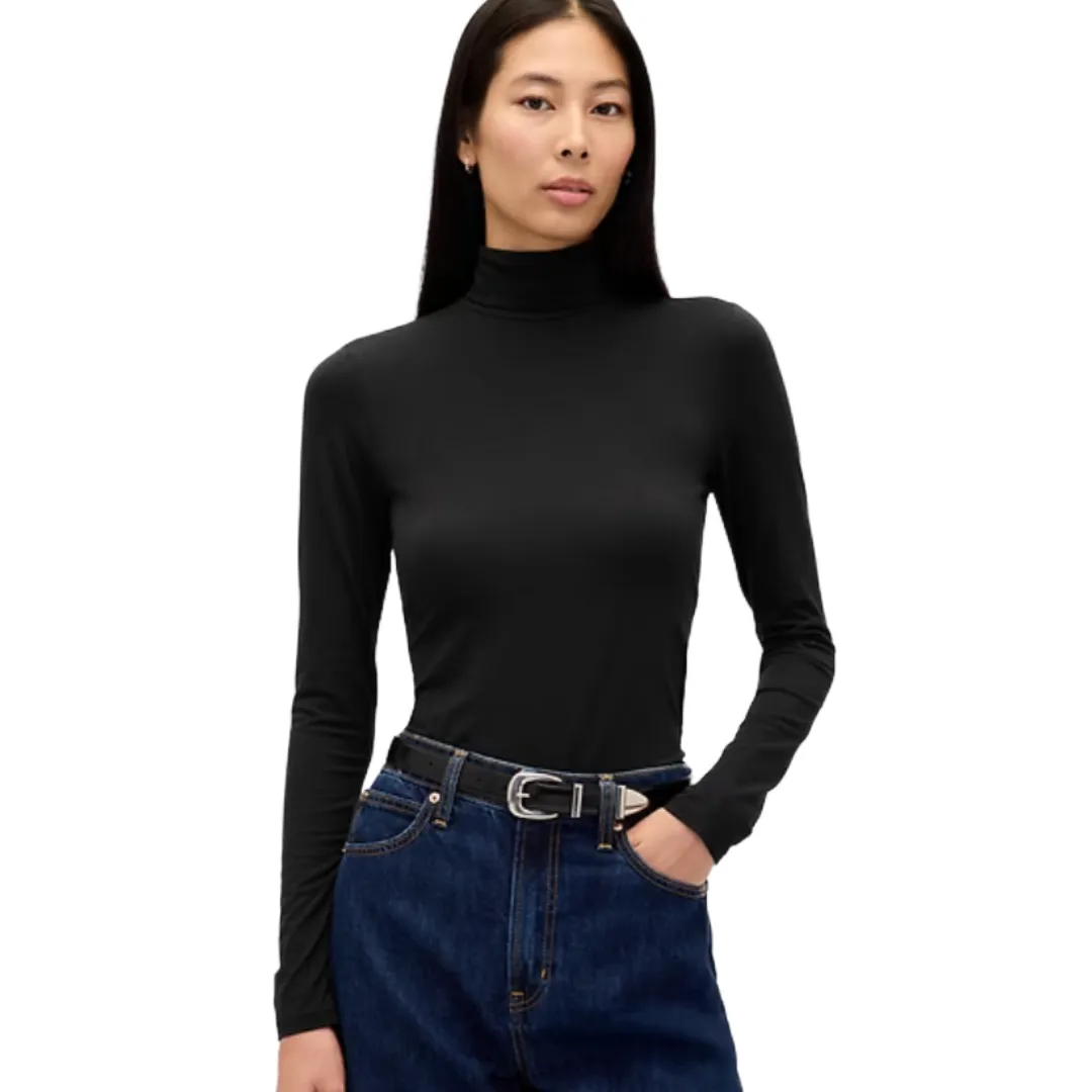 A woman is wearing a black long-sleeve turtleneck top paired with high-waisted blue jeans and a black belt, standing against a plain white background.