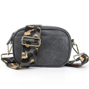 A small black crossbody bag with a gold clasp and a detachable strap featuring a camouflage pattern in black and tan.