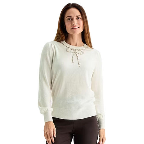 White long-sleeve sweater with beaded bow detail at the neckline, paired with dark pants.
