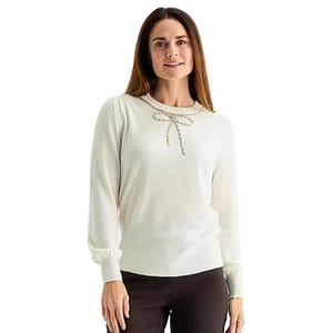 White long-sleeve sweater with beaded bow detail at the neckline, paired with dark pants.