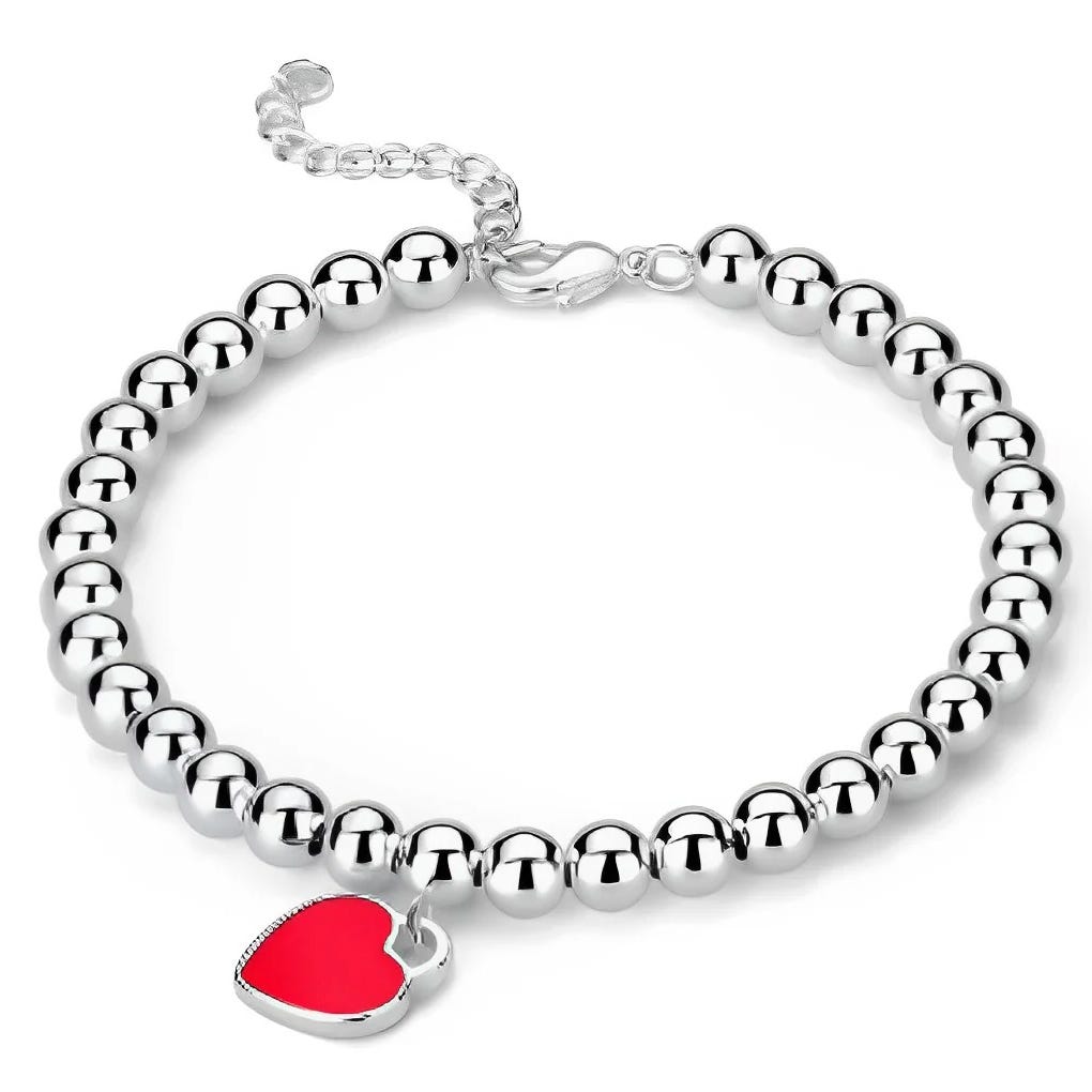A bracelet made of shiny silver beads features a red heart charm and an adjustable chain clasp.