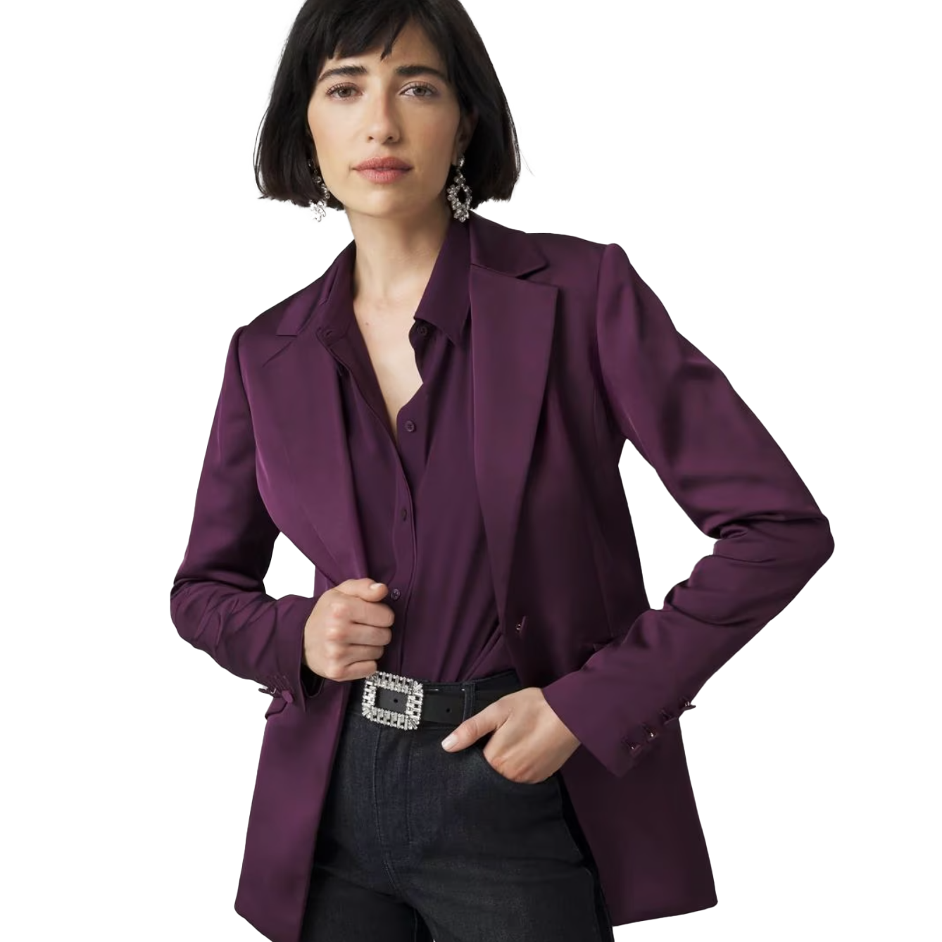 A woman is wearing a WHBM Fully-Lined Blazer in a deep purple color, paired with a matching shirt and dark jeans. The blazer is styled with a decorative belt and statement earrings.