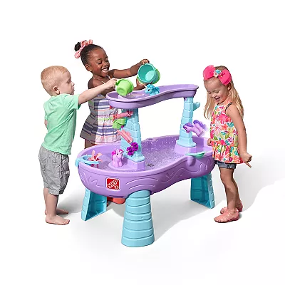 Three children are playing with a purple and blue water table that has a variety of water toys and accessories on it.