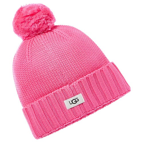 A bright pink knit beanie from UGG featuring a pom-pom on top and a rolled cuff with a small UGG logo tag on the front.