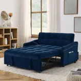 Blue upholstered sofa bed with a pull-out sleeper design. Features a side pocket and nailhead trim, positioned in a cozy living room setup with a window, rug, and bookshelf.