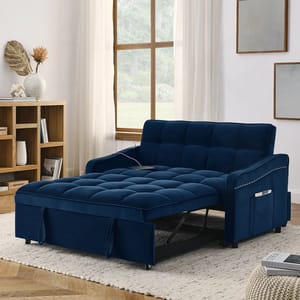 Blue upholstered sofa bed with a pull-out sleeper design. Features a side pocket and nailhead trim, positioned in a cozy living room setup with a window, rug, and bookshelf.