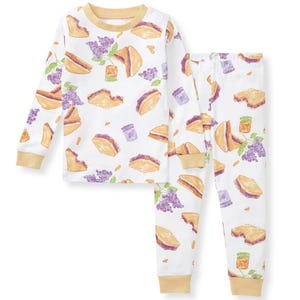 A children's pajama set featuring a whimsical pattern of peanut butter and jelly sandwiches, jars, and grapes on a white background with beige cuffs.