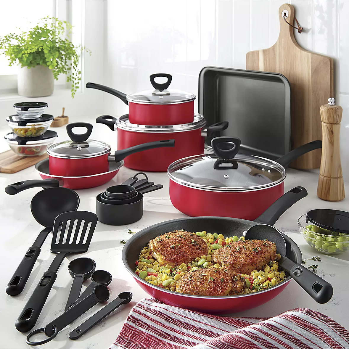 Red cookware set with pots, pans, lids, and kitchen utensils on a kitchen counter.