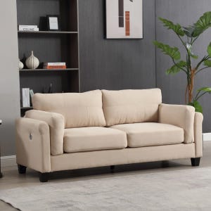 A beige two-seater sofa with plush cushions is situated in a modern living room featuring a gray wall, bookshelf, abstract art, and a potted plant.