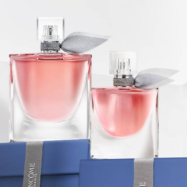 Two bottles of pink perfume with silver leaf-shaped accents, resting on blue boxes.