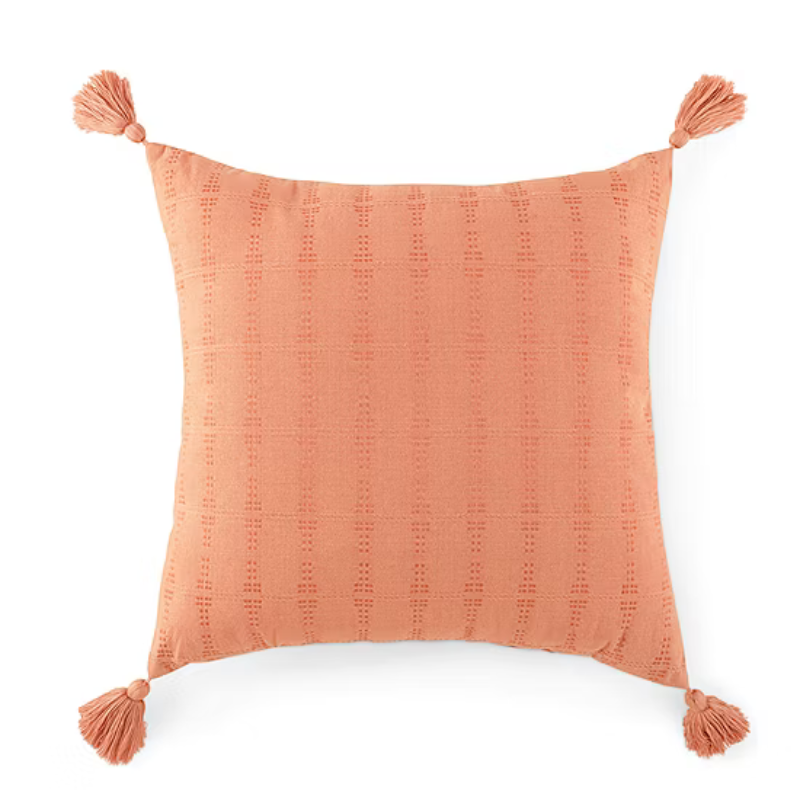 Square coral pillow with a subtle pattern and tassels on each corner.