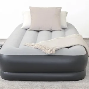 An inflatable air mattress with a gray and black design is topped with three pillows and a fringed throw blanket, situated on a gray carpet.
