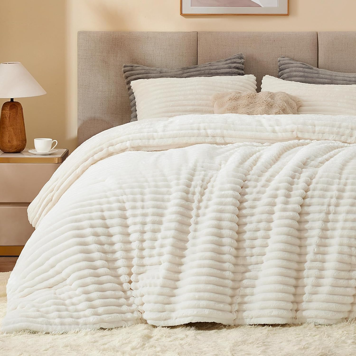 A cozy, textured bedding set with a plush, ribbed white comforter and matching pillows, complemented by a wooden nightstand with a lamp and cup, situated in a neutral-toned bedroom.
