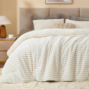 A cozy, textured bedding set with a plush, ribbed white comforter and matching pillows, complemented by a wooden nightstand with a lamp and cup, situated in a neutral-toned bedroom.