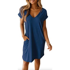 A woman is wearing a casual blue V-neck short-sleeve shirt dress with pockets. The dress has a relaxed fit and is made for summer wear, complemented by earrings and a bracelet.