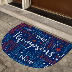 A personalized doormat with a blue background features the family name \“Thompsons\“ prominently, surrounded by the names Jake, Elijah, Emily, Nate, and various stars in red and white.