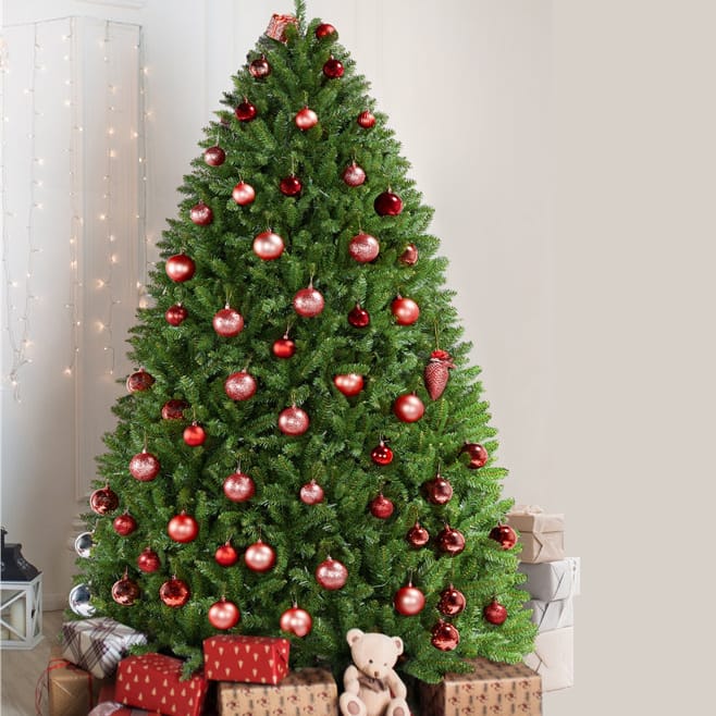 A 6-foot ultra-thick Christmas tree decorated with red and gold ornaments and surrounded by wrapped gifts and a small teddy bear at its base. White string lights are hung in the background for added ambiance.