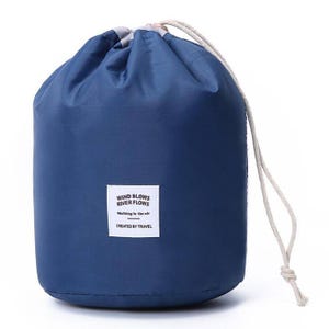 A blue drawstring bag with a label reading \“WIND BLOWS RIVER FLOWS, Walking in the air, CREATED BY TRAVEL.\“
