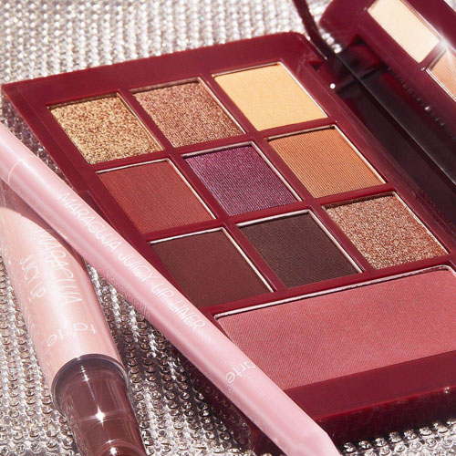 A palette with 12 eyeshadows in warm tones, including mattes and shimmers, is shown alongside two pencil products, likely eyeliners or lip pencils, in coordinating colors.