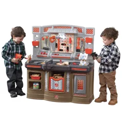 Children are playing with a toy workbench set featuring tools like a drill, saw, pliers, and a vise, along with a small wooden house project.