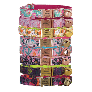 Stack of colorful pet collars with floral patterns, each featuring a metal buckle engraved with names like \“Andy,\“ \“Piper,\“ and \“Shark,\“ along with contact numbers.