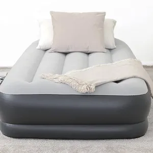 Gray and black inflatable air mattress with a soft top surface, featuring two pillows and a fringed throw blanket, placed on a carpeted floor.
