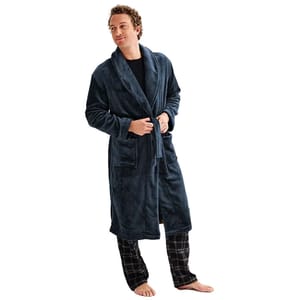 A man is wearing a dark blue, plush Sonoma robe with a shawl collar, tied at the waist, and featuring two front pockets. He also wears plaid pajama pants and stands barefoot.