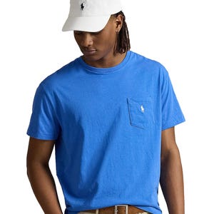 Man wearing a blue T-shirt with a chest pocket and a white logo, paired with a white cap featuring a similar logo.
