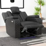 A black reclining chair with diamond-pattern stitching and an adjustable footrest is set on a modern rug, surrounded by a potted plant, a lamp, and a side table, creating a cozy living space.