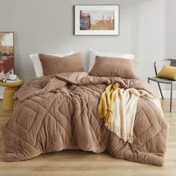 Cozy bedroom setup with a textured brown comforter, matching pillows, a contrasting yellow and white throw, and abstract artwork. Includes a side table with a decorative piece and a modern chair with a yellow cushion.