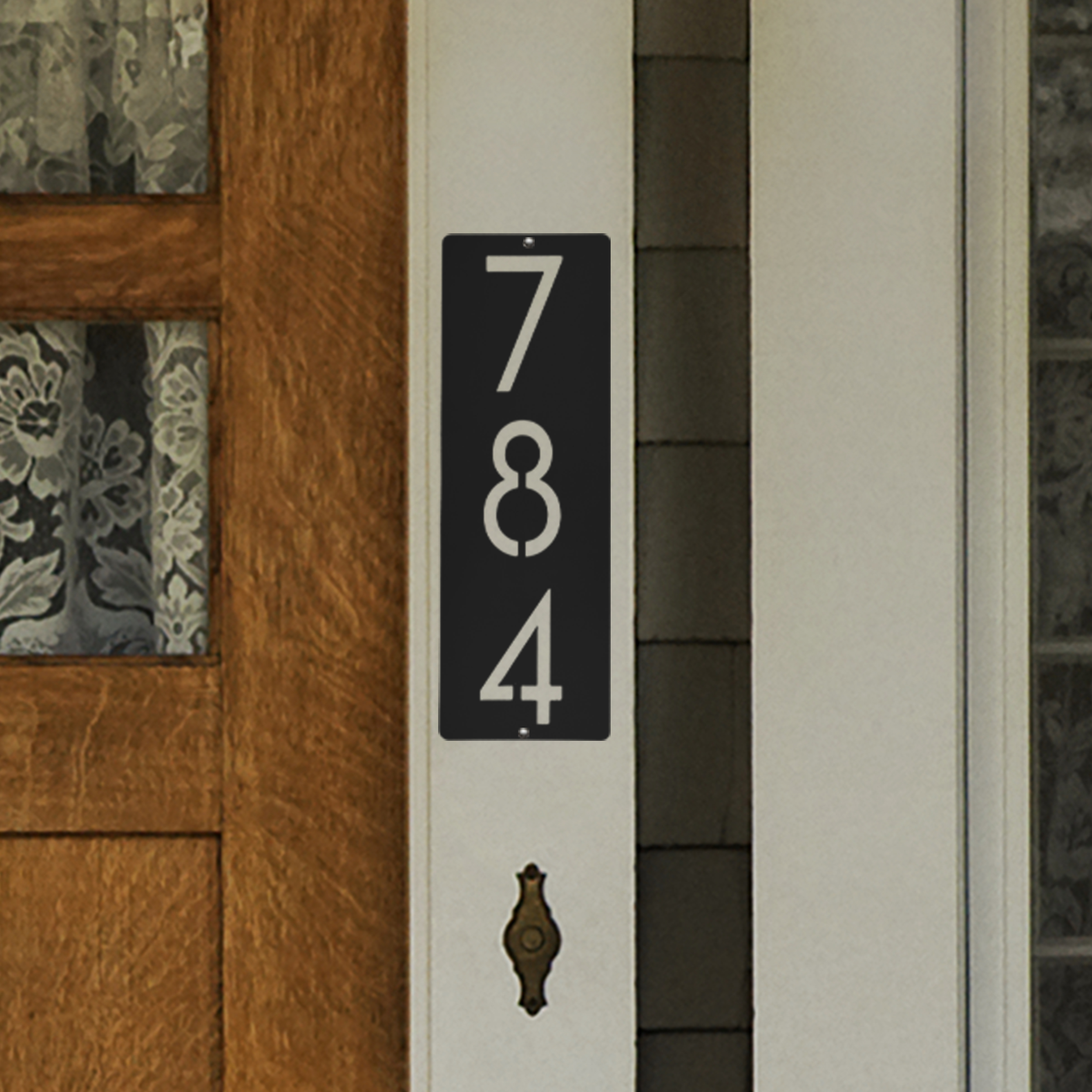 Vertical house number sign with the digits 7, 8, and 4 displayed on a black background, mounted beside a wooden door with lace curtains.
