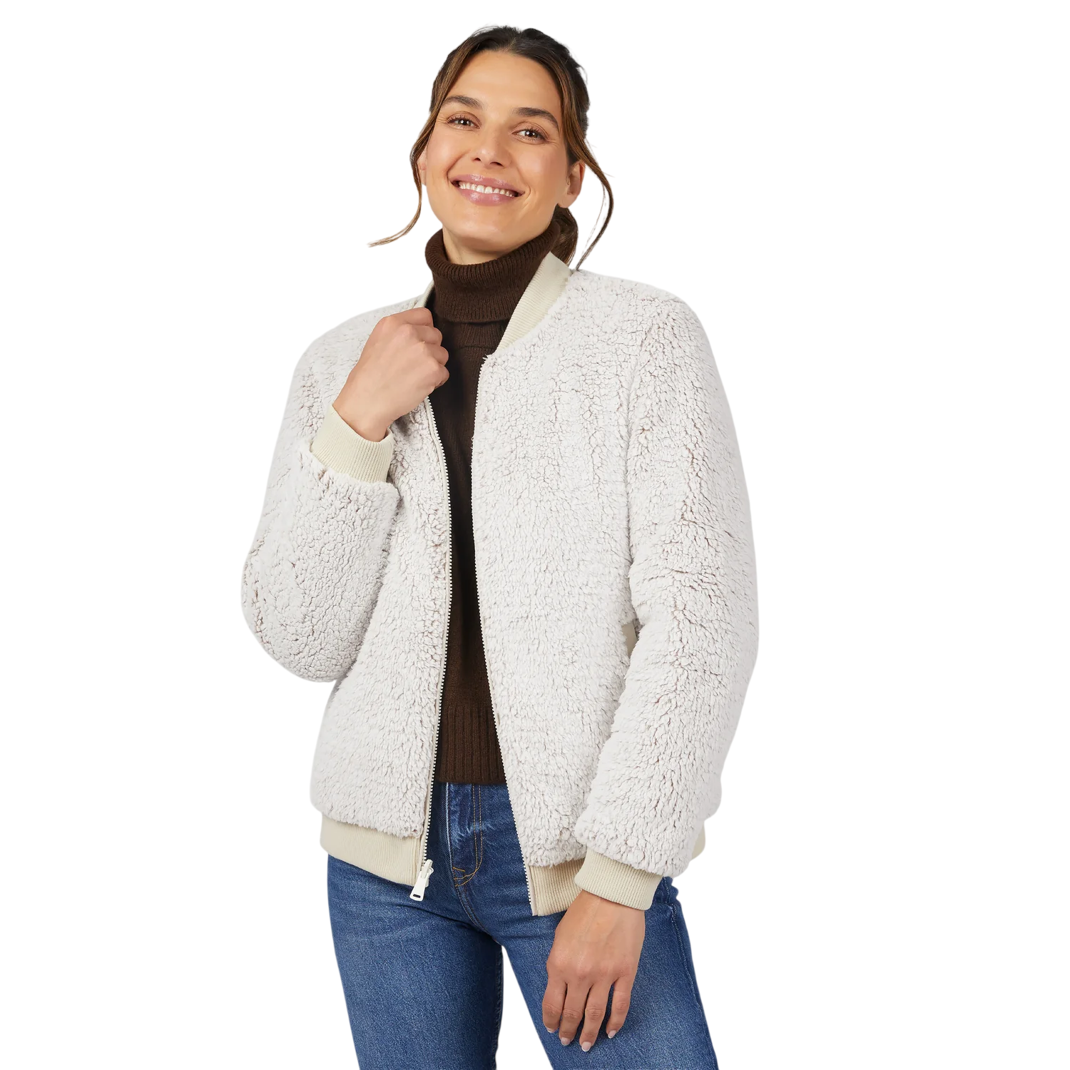 A woman wears a white, textured bomber jacket over a dark brown turtleneck and blue jeans, smiling with one hand touching the jacket.