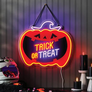 Neon pumpkin sign with \“Trick or Treat\“ message, accompanied by black candles and a mummy-themed candy holder filled with sweets.