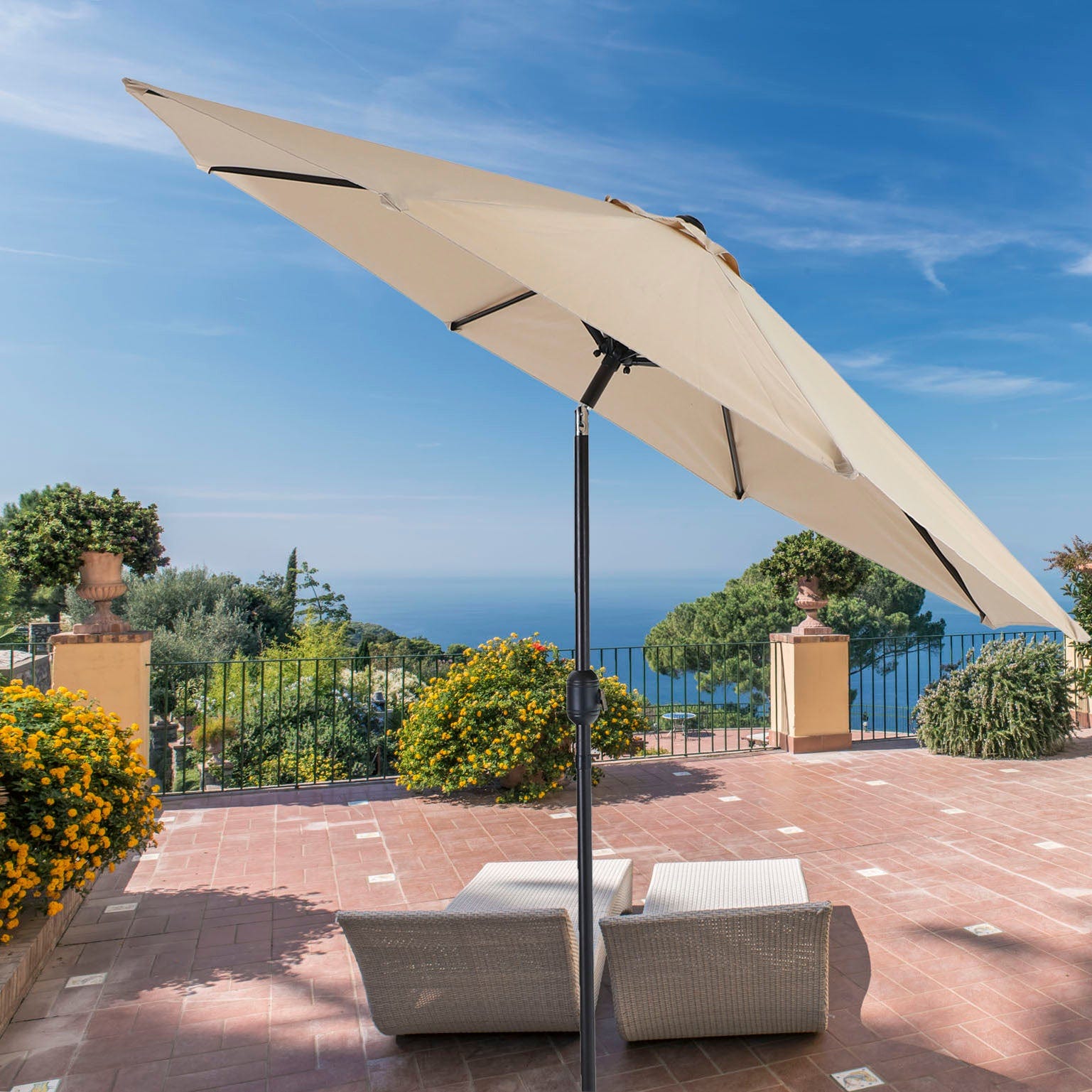 Offset patio umbrella with a cantilever design, accompanied by outdoor wicker chairs, on a terrace overlooking the sea.