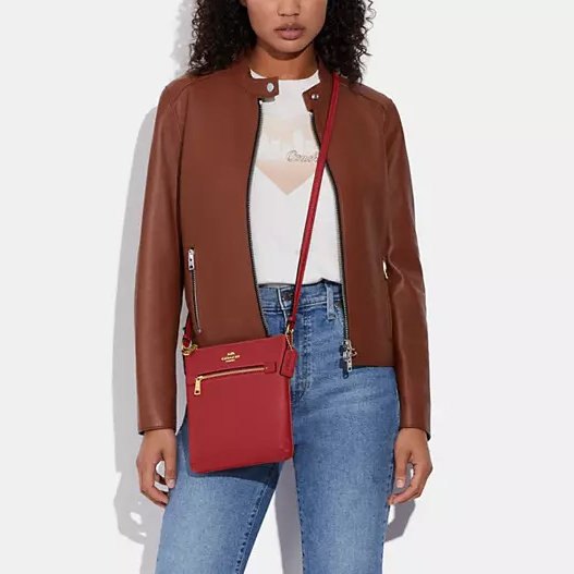 A woman wearing a brown leather jacket, white top, blue jeans, and carrying a red shoulder bag.