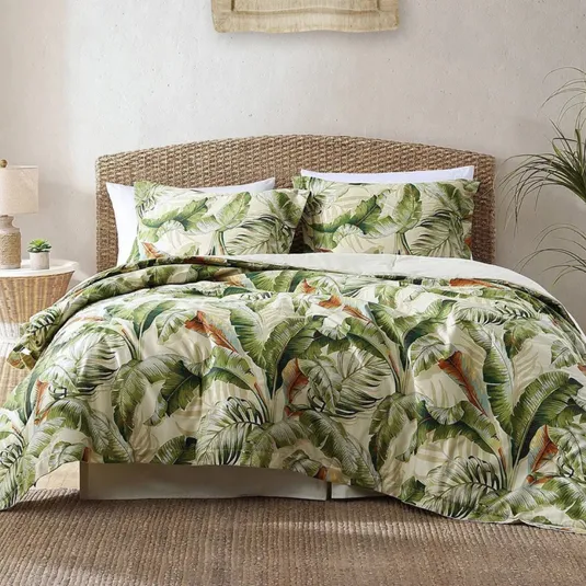 A bedding set with a banana leaf print, featuring a woven headboard, a side table with a lamp, and a small plant.