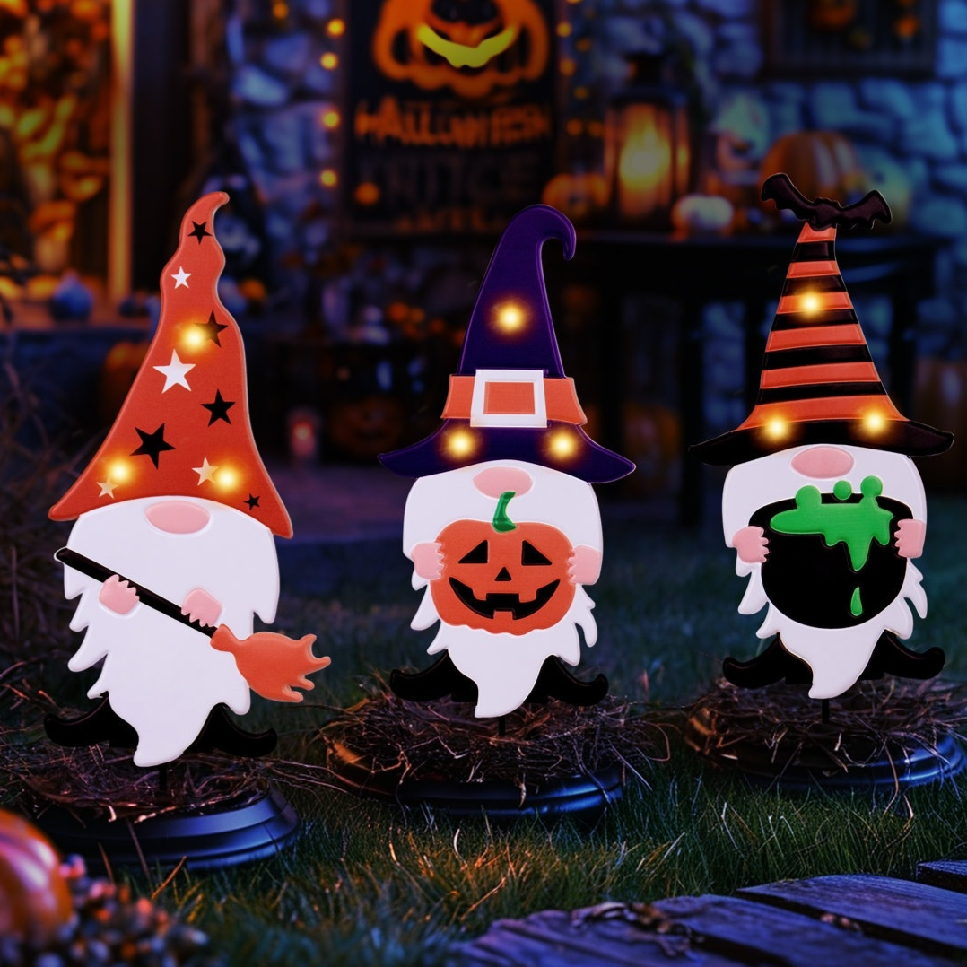 Three Halloween-themed gnome decorations are displayed, each with a distinct hat design and holding items like a broom, a jack-o'-lantern, and a cauldron, all illuminated with small lights.