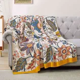 A vibrant floral-patterned blanket with blue, yellow, and orange hues is draped over a gray tufted sofa, adding a decorative touch to the living room setting.