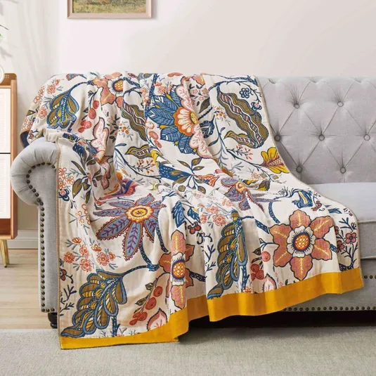 A vibrant floral-patterned blanket with blue, yellow, and orange hues is draped over a gray tufted sofa, adding a decorative touch to the living room setting.