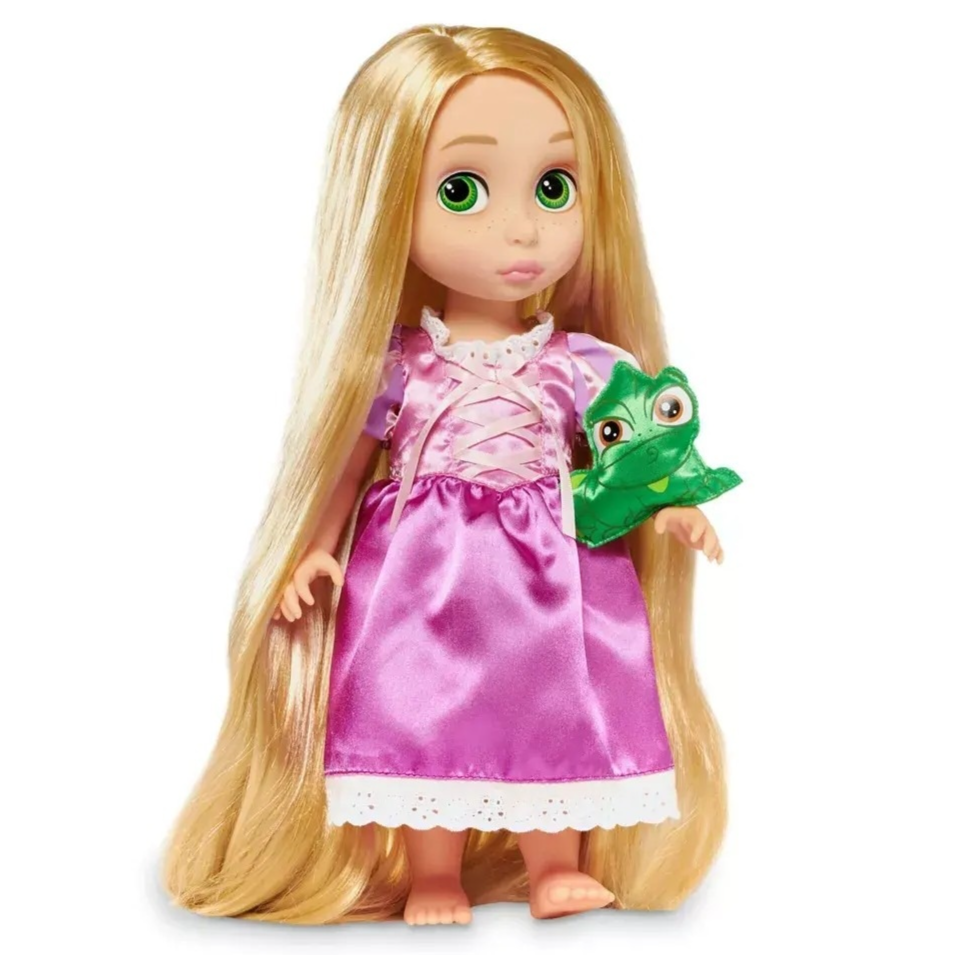 A doll with long blonde hair dressed in a pink and purple outfit, holding a green chameleon plush toy.