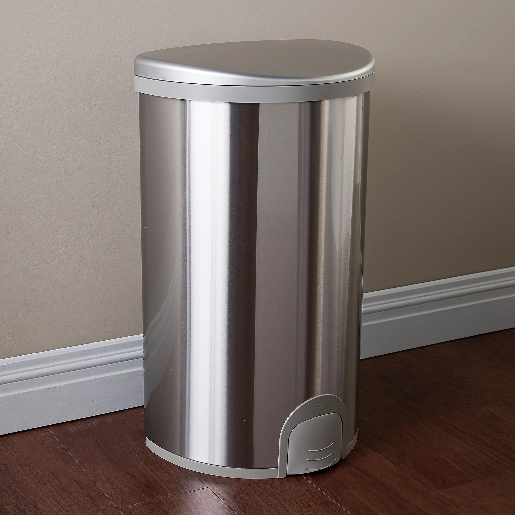 A sleek, semi-circular trash can with a brushed metallic finish, featuring a foot pedal for hands-free operation.
